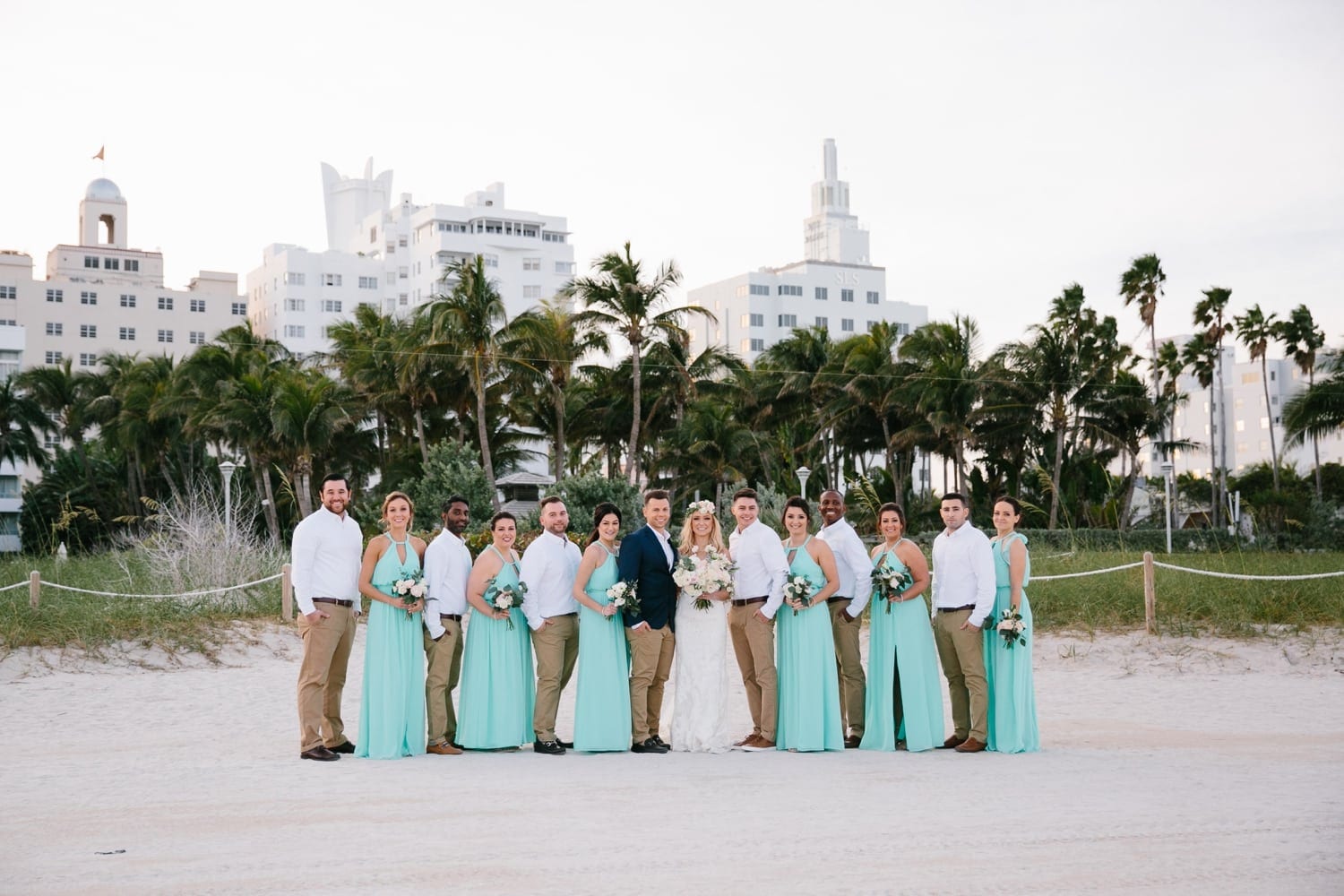 Wedding party Portrait. Turquoise bridesmaids dresses. Khaki pants and Blue Jacket Suit. Winter Beach Wedding at the National Hotel in South Beach Fl